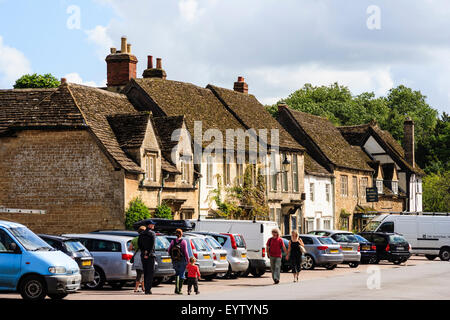 England, Lacock, Cotswolds. Blick entlang der High Street mit seinen 17. Jahrhundert Stein Häuser und Gebäude, Autos geparkt und Touristen umher. Stockfoto