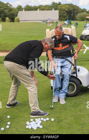 Mann mit einer Rückenmarksverletzung in eine adaptive Warenkorb bei Golf-Putting-Green mit einem Instruktor Stockfoto