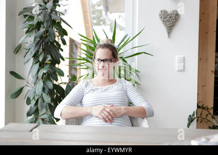 eine schwangere blonde Frau mit Brille sitzt an einem Tisch Stockfoto