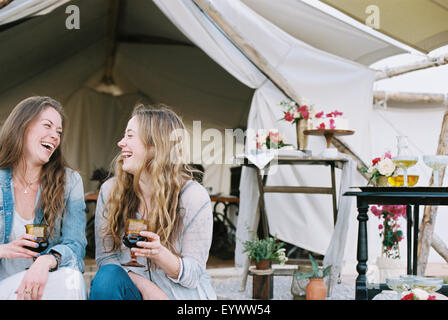Zwei lächelnde Frauen sitzen vor einem Zelt in der Wüste bei einem Glas Wein. Stockfoto
