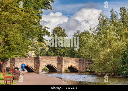 Ein Mann auf der Suche auf seine Uhr, als er neben dem Fluss Wye Spaziergänge, gebaut vor 5 Bogenbrücke vor 700 Jahren Bakewell, Derbyshire... Stockfoto