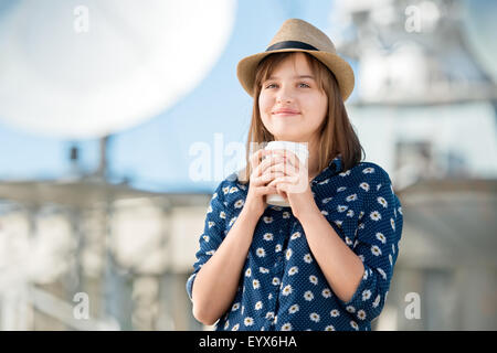 Glückliche junge Frau hält Kaffee zum mitnehmen und posieren vor Hintergrund der parabolischen Satellitenschüsseln, die Wireless-Zeichen erhalten Stockfoto