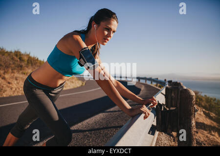 Junge Sportlerin stützte sich auf Autobahn Leitplanke wegsehen. Frau Läufer im Freien auf der Landstraße eine Pause nach runni Stockfoto