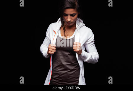 Porträt von Fit junge Frau in Sportbekleidung steht auf schwarzem Hintergrund schaut. Kaukasische Fitness-Modell hält ihr sweatsh Stockfoto