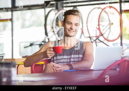 Lächelnder Mann Kaffeetrinken am Laptop im Bike-shop Stockfoto