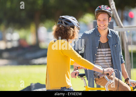 Mann und Frau mit Fahrrädern, Helmen und sprechen im park Stockfoto