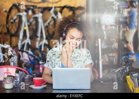Lächelnde Frau mit Kopfhörern arbeiten am Laptop im Fahrradgeschäft Stockfoto