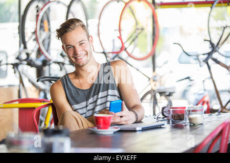 Porträt, Lächeln Mann mit Kaffee und Handy im Fahrradgeschäft Stockfoto