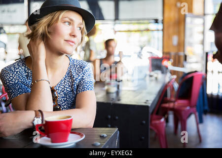 Nachdenkliche Frau mit Hut mit Kaffee im Café wegschauen Stockfoto