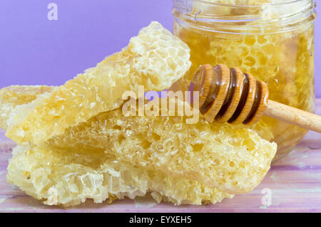 Waben Sie-Dipper und Glas Honig auf lila Hintergrund Stockfoto