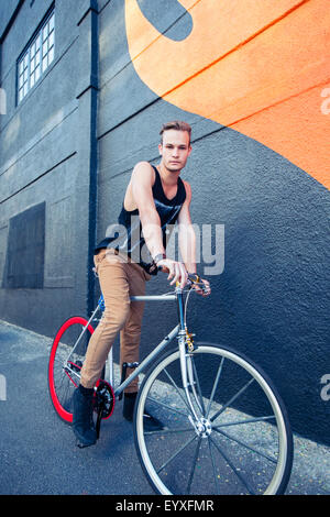 Porträt ernst junger Mann auf dem Fahrrad neben urban Graffitiwand Stockfoto