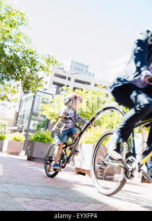 Sohn im Helm Tandem Fahrrad mit Geschäftsmann Vater im sonnigen Stadtpark Stockfoto