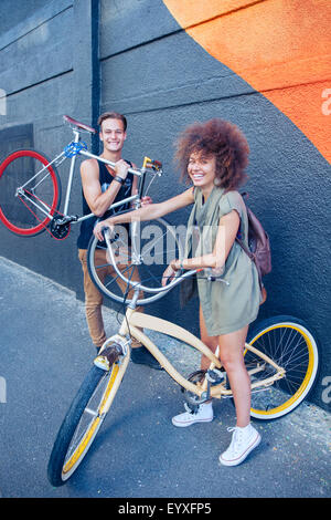 Porträt, Lächeln Freunde mit Fahrrädern neben städtischen Wand Stockfoto