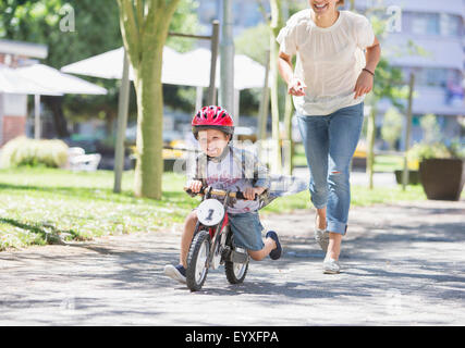 Mutter Jagd Sohn Fahrrad mit Helm im sonnigen park Stockfoto