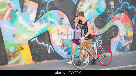 Junges Paar mit Fahrrad umarmt und städtische multicolor Graffiti-Wand entlang Stockfoto