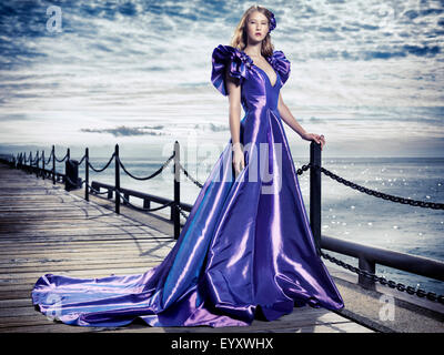 Junge Frau trägt ein schönes langes blaues Abendkleid steht im Waterfront, künstlerische Mode Porträt