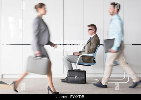 Unternehmer Arbeiten am Laptop in der Lobby hinter Geschäftsleute, die viel unterwegs sind Stockfoto
