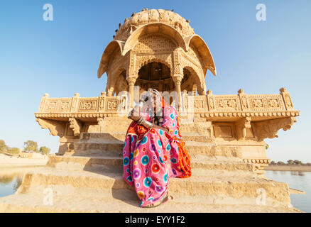 Indische Frau in traditioneller Kleidung, die sitzt in der Nähe von Denkmal, Jaisalmer, Rajasthan, Indien Stockfoto