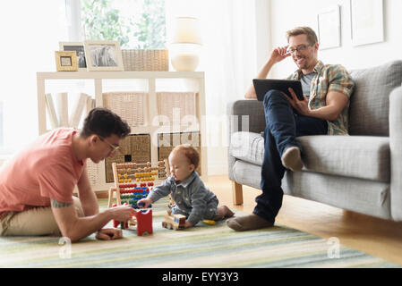 Kaukasische Schwule Väter und Baby im Wohnzimmer entspannen Stockfoto