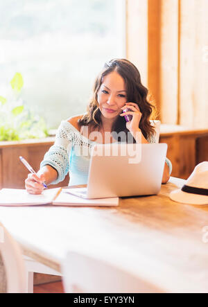 Chinesische Frau auf Handy mit Laptop im café Stockfoto