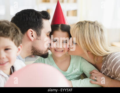 Kaukasische Eltern küssen Tochter auf Geburtstagsparty Stockfoto