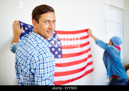 Lächelnder Mann, Blick in die Kamera auf Grund seines Sohnes USA-Flagge an Wand hängen Stockfoto