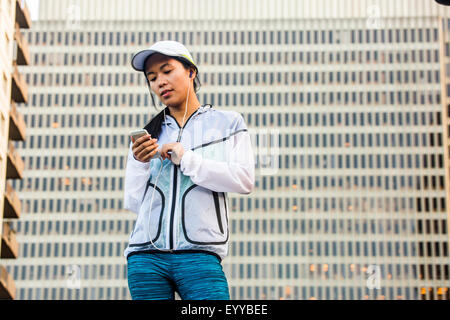 Asiatische Läufer mit Handy in der Nähe von Hochhaus Stockfoto