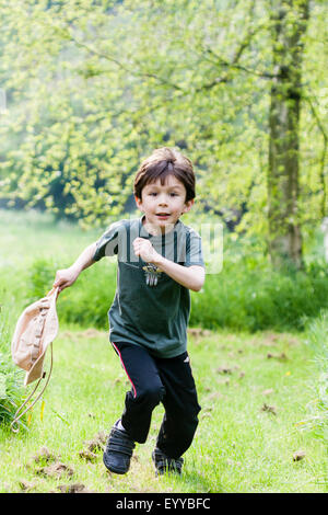 Kaukasier Kind, Braunhaariger Junge, 7- bis 8-Jährigen, draußen laufen in Richtung Betrachter, Schlapphut, zusammen Gras weg in das Waldgebiet, Lachen. Stockfoto