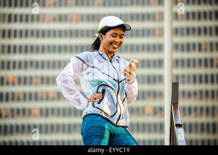 Asiatische Läufer mit Handy in der Nähe von Hochhaus Stockfoto