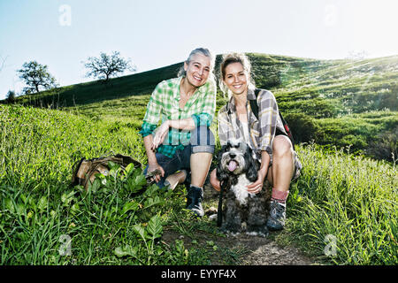 Kaukasische Mutter und Tochter gehen Hunde auf grasbewachsenen Hang Stockfoto