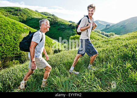 Kaukasische Vater und Sohn gehen auf grasbewachsenen Hang Stockfoto