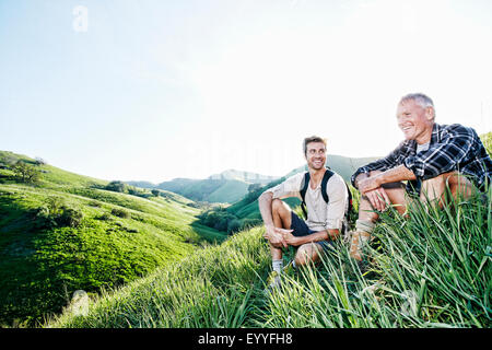 Kaukasische Vater und Sohn sitzen auf grasbewachsenen Hang Stockfoto