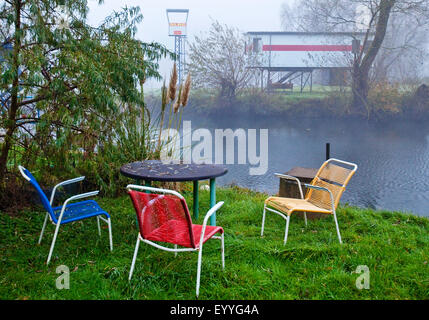 bunte Gartenstühle am Ufer Ruhr Flusses im herbstlichen Nebel, Witten, Ruhrgebiet, Nordrhein-Westfalen, Deutschland Stockfoto