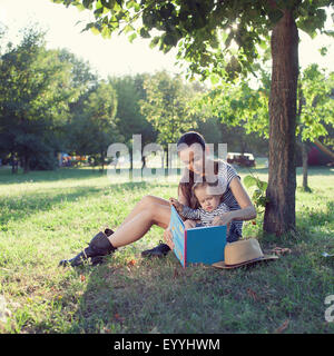 Junge stilvolle Mutter und Kleinkind Lesebuch im Garten im Sommer-Spaß Stockfoto