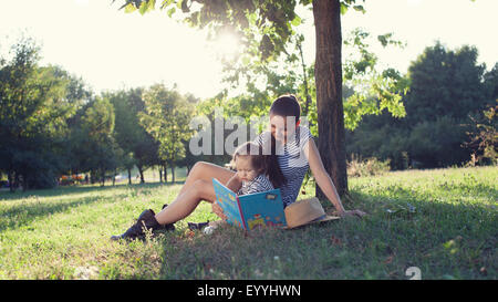 Junge stilvolle Mutter und Kleinkind Lesebuch im Garten im Sommer-Spaß Stockfoto