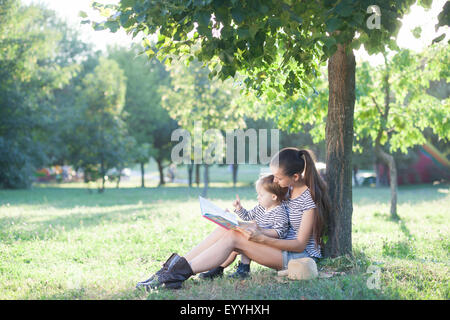 Junge stilvolle Mutter und Kleinkind Lesebuch im Garten im Sommer-Spaß Stockfoto