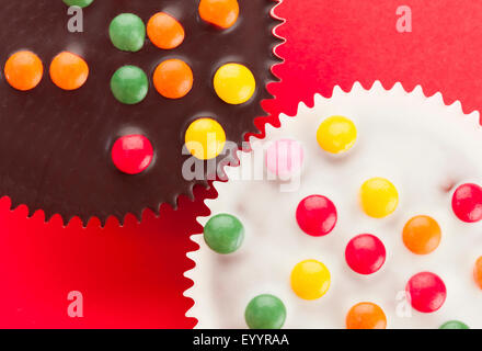 Nahaufnahme der Cupcakes ähnlich wie Zahnräder, mit dunklen und weißen Schokoladenglasur verziert mit Smarties, auf rotem Grund, Ansicht von oben, Stockfoto