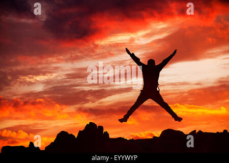 Sonnenuntergang über Loughrigg in Ambleside, Lake District, Großbritannien, mit einem Mann springen vor Freude. Stockfoto