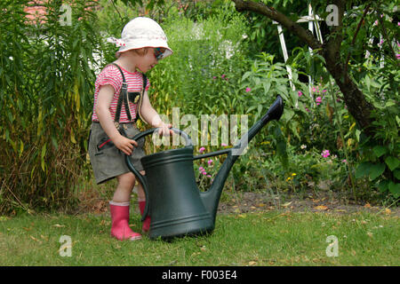 kleines Mädchen in Lederhosen spielen im Garten mit der Gießkanne, Deutschland Stockfoto