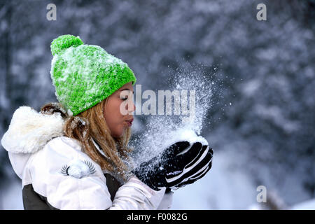 fröhliche gut aussehende junge Frau bläst im Schnee in ihr Hände, Frankreich, Savoie Stockfoto