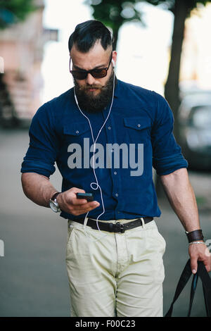 bärtiger Mann geht und hört Musik Stockfoto