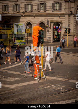 Arbeiter Kleidung Warnschutz orange Befestigung Ampel mitten in einer belebten Straße in Rom. Italien. Stockfoto