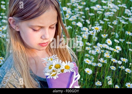 Blonde kaukasische Mädchen hält einen lila Sneaker gefüllt mit wilden Gänseblümchen auf einer Wiese. Stockfoto