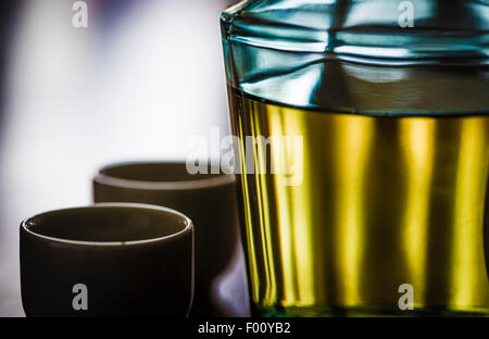 Eine Flasche des japanischen alkoholischen trinken Sake und Sake Keramikbechern im Gegenlicht auf einem dunklen Holztisch. Stockfoto