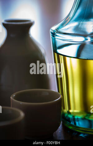 Eine Flasche des japanischen alkoholischen trinken Sake und Sake Keramikbechern im Gegenlicht auf einem dunklen Holztisch. Stockfoto