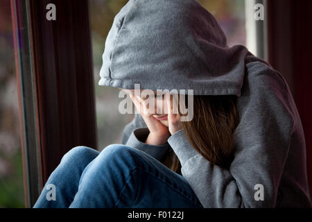 Trauriges Mädchen in Kapuzenshirt, sitzen mit dem Gesicht in den Händen in Verzweiflung Stockfoto