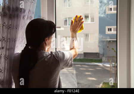junge Frau, die Reinigung der Fenster mit gelben Lappen innen Stockfoto