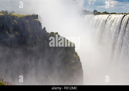 Viktoriafälle vom Mosi-Oa-Tunya Nationalpark in Sambia. Besucher auf der Klippe gegenüber sind auf der Zimbabwe Seite Stockfoto