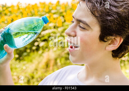 Umweltfreundliche wohnen - kaukasischen junge in einem Feld von Sonnenblumen soll klares Wasser aus einem Kunststoff Flaschengrün bläulich, an einem warmen und hellen Sommertag Durst trinken Stockfoto