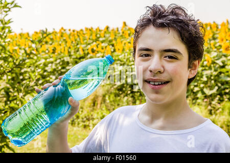 Umweltfreundliche wohnen - kaukasischen junge in einem Feld von Sonnenblumen soll klares Wasser aus einem Kunststoff Flaschengrün bläulich, an einem warmen und hellen Sommertag Durst trinken Stockfoto